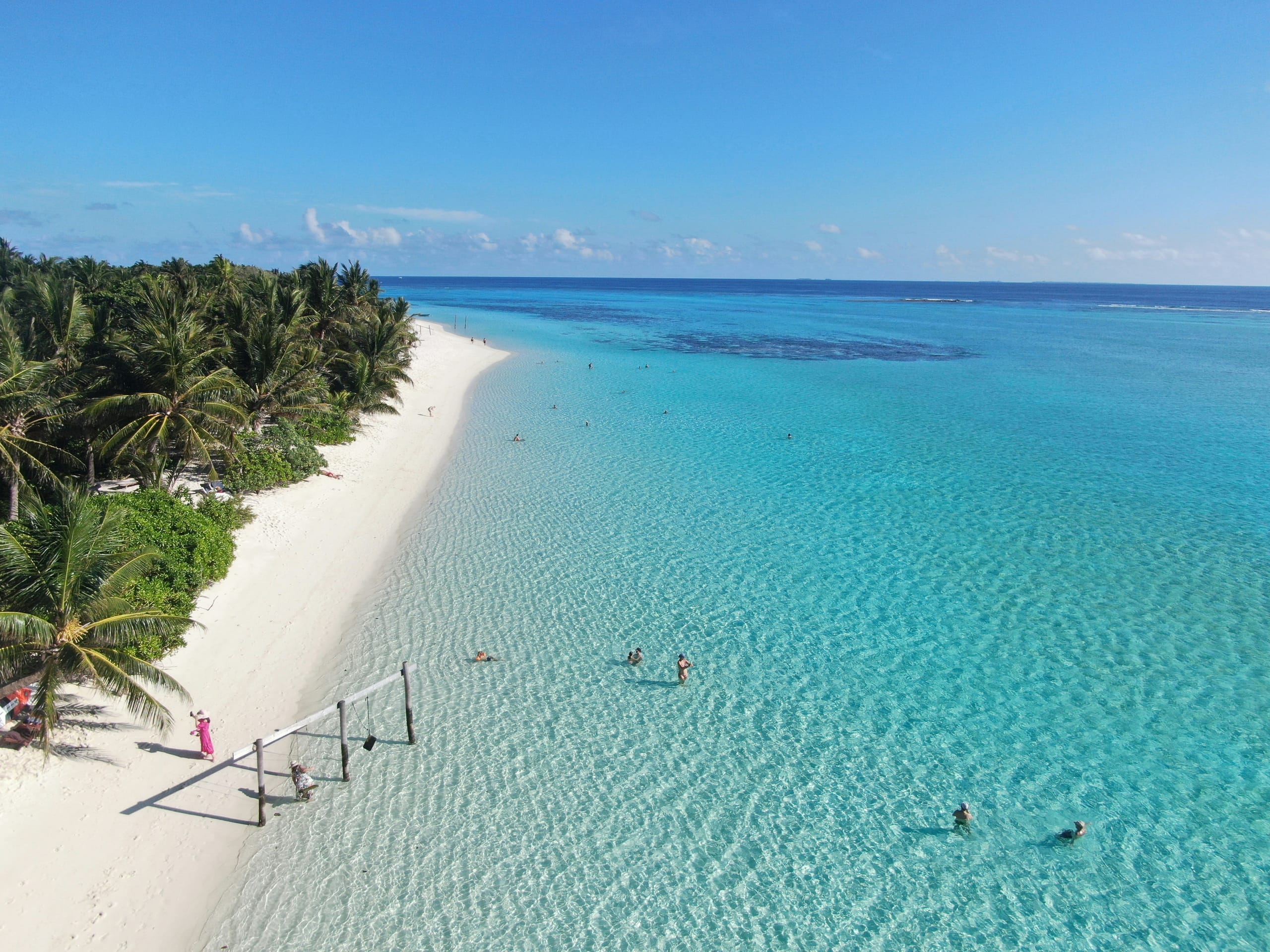 A white sand spit on Thoddoo in the Maldives seen from above, a volleyball net standing at the waterline and people swimming in the clear shallows
