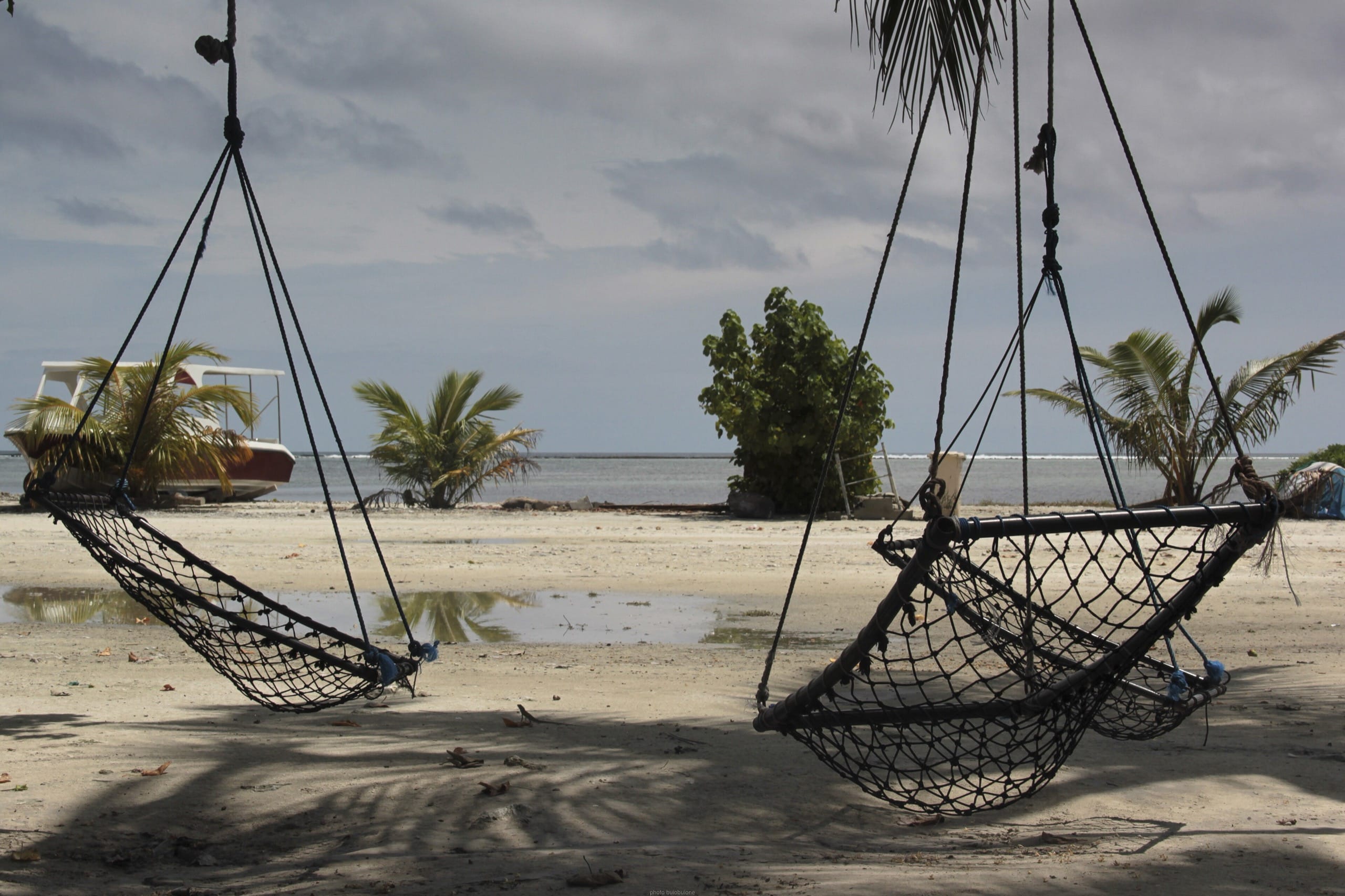 Two empty rope hammocks on a sandy shore on Maafushi with a boat behind