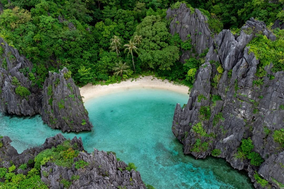 Secret Beach at El Nido seen from above, a small white sand cove enclosed by limestone spires and jungle
