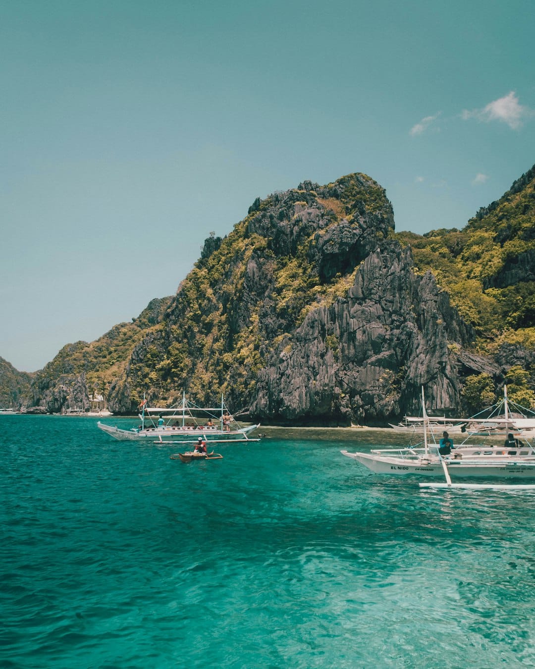 Outrigger tour boats moored in green water below a limestone island at El Nido