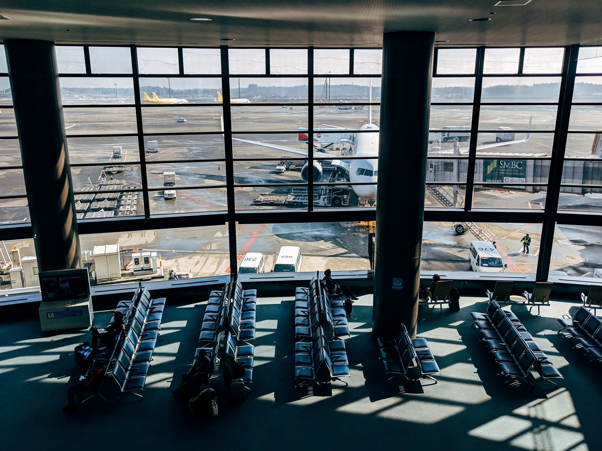 An airport gate lounge with rows of empty seats, sunlight across the floor and a jet parked at the gate outside