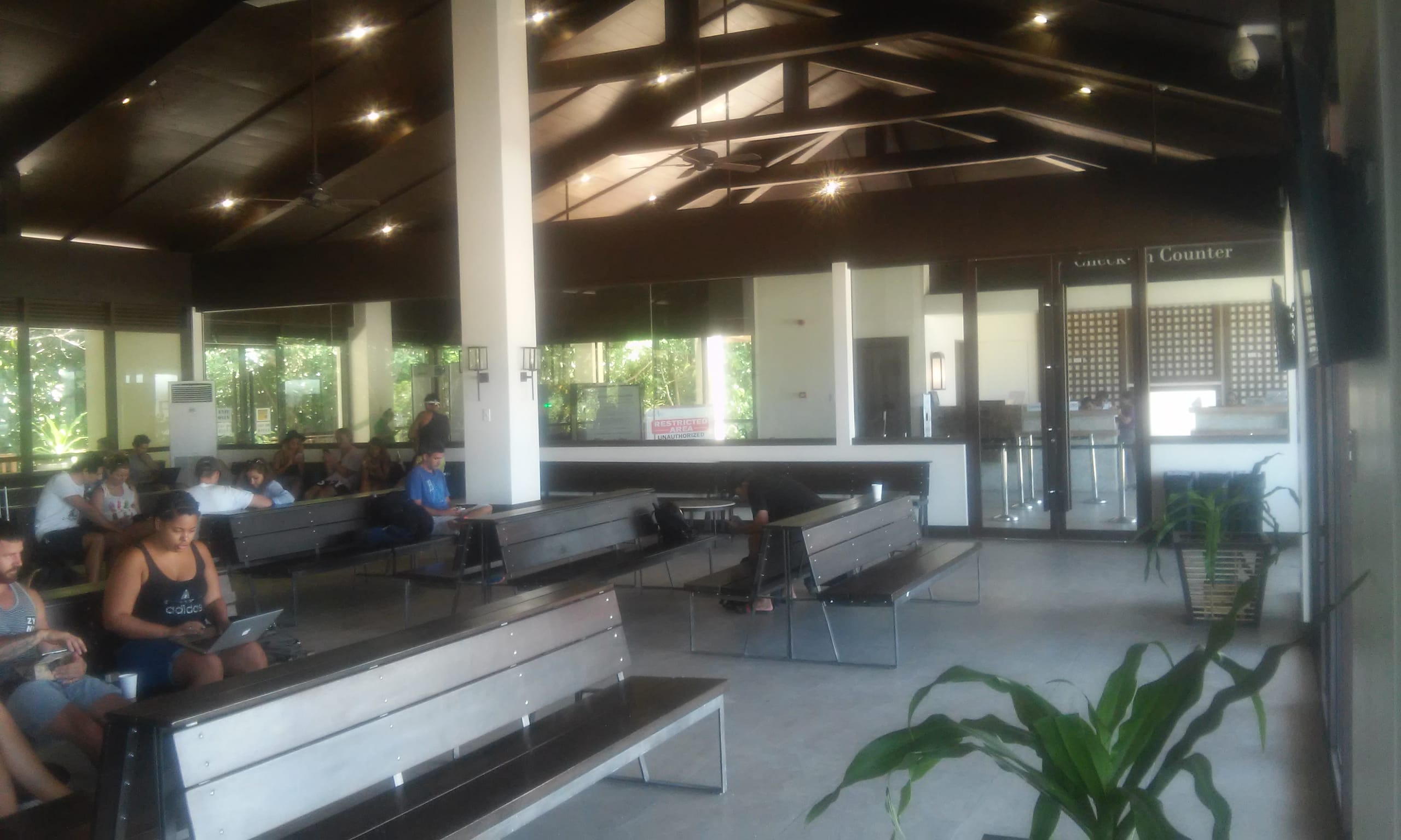 Dark-beamed terminal at El Nido airport with benches, seated travelers and the check-in counter behind glass