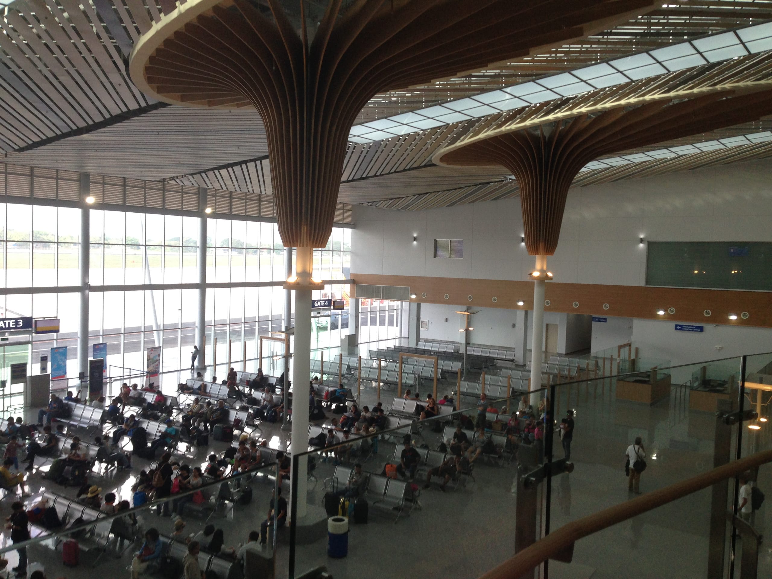 Departure hall of Puerto Princesa airport, rows of seated passengers under tree-shaped wooden ceiling columns