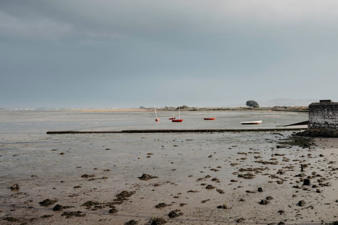 Small boats aground on a grey tidal flat at low tide in Ireland under a heavy sky, a low sea wall at the right