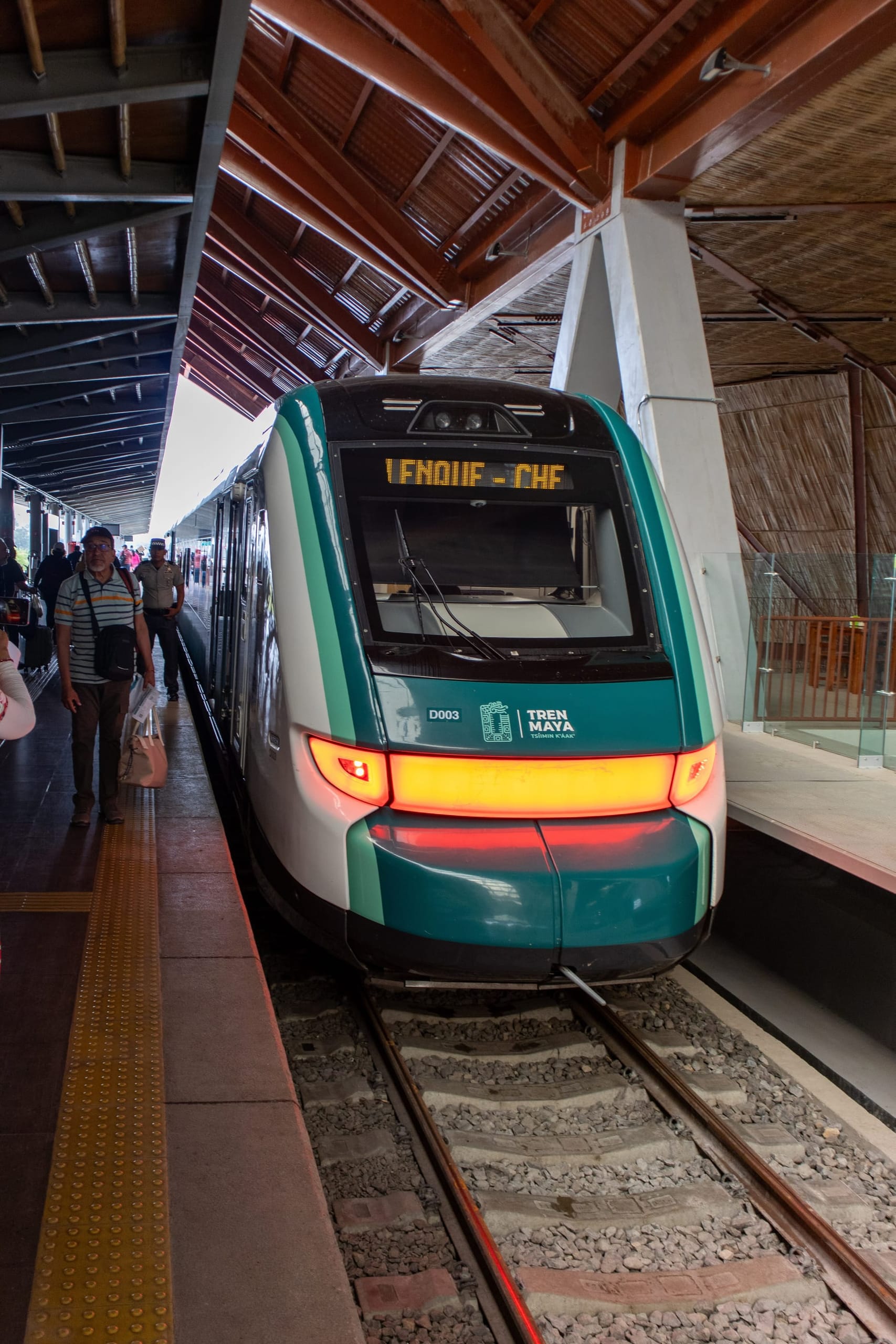 A Tren Maya train standing at a platform under a timber canopy, passengers walking alongside