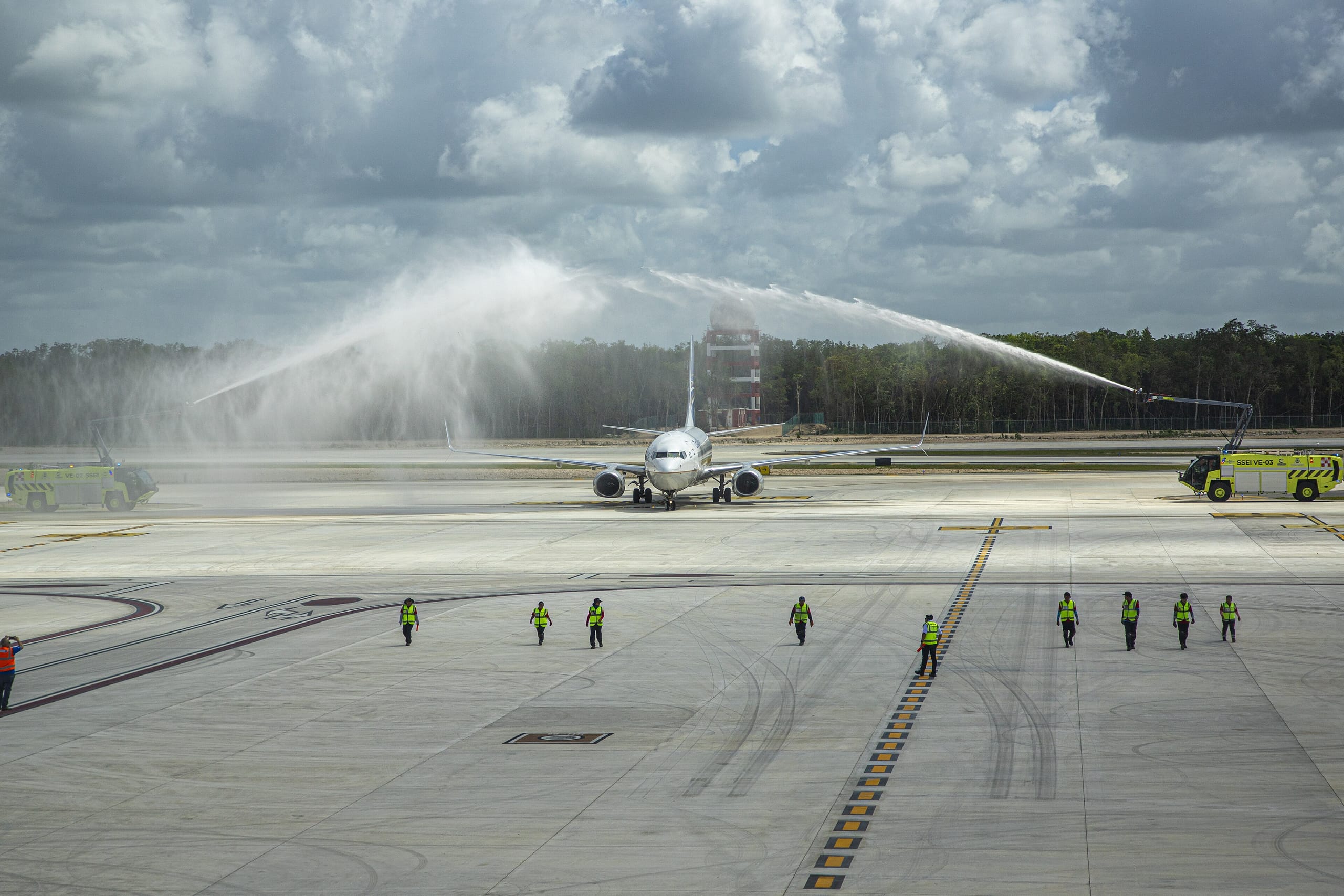 Jet on the Tulum airport apron greeted by a water cannon salute, forest behind