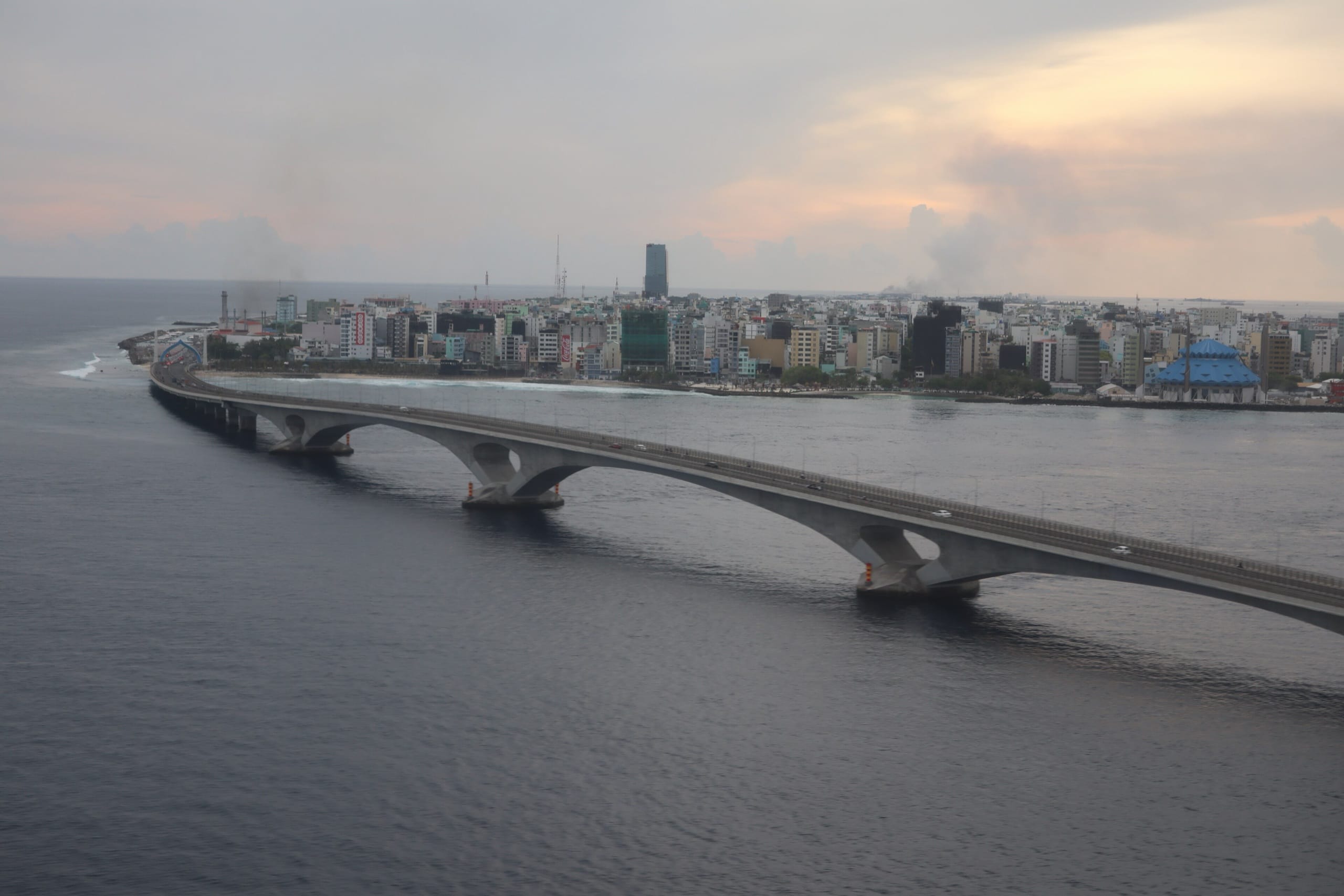 The Sinamalé Bridge arching low over open water toward the packed skyline of Malé at dusk