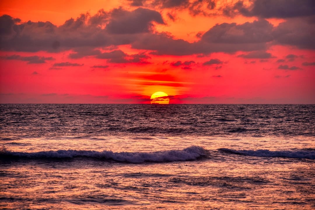 The sun going down into the sea under a red sky at Acapulco, a low wave breaking in the foreground