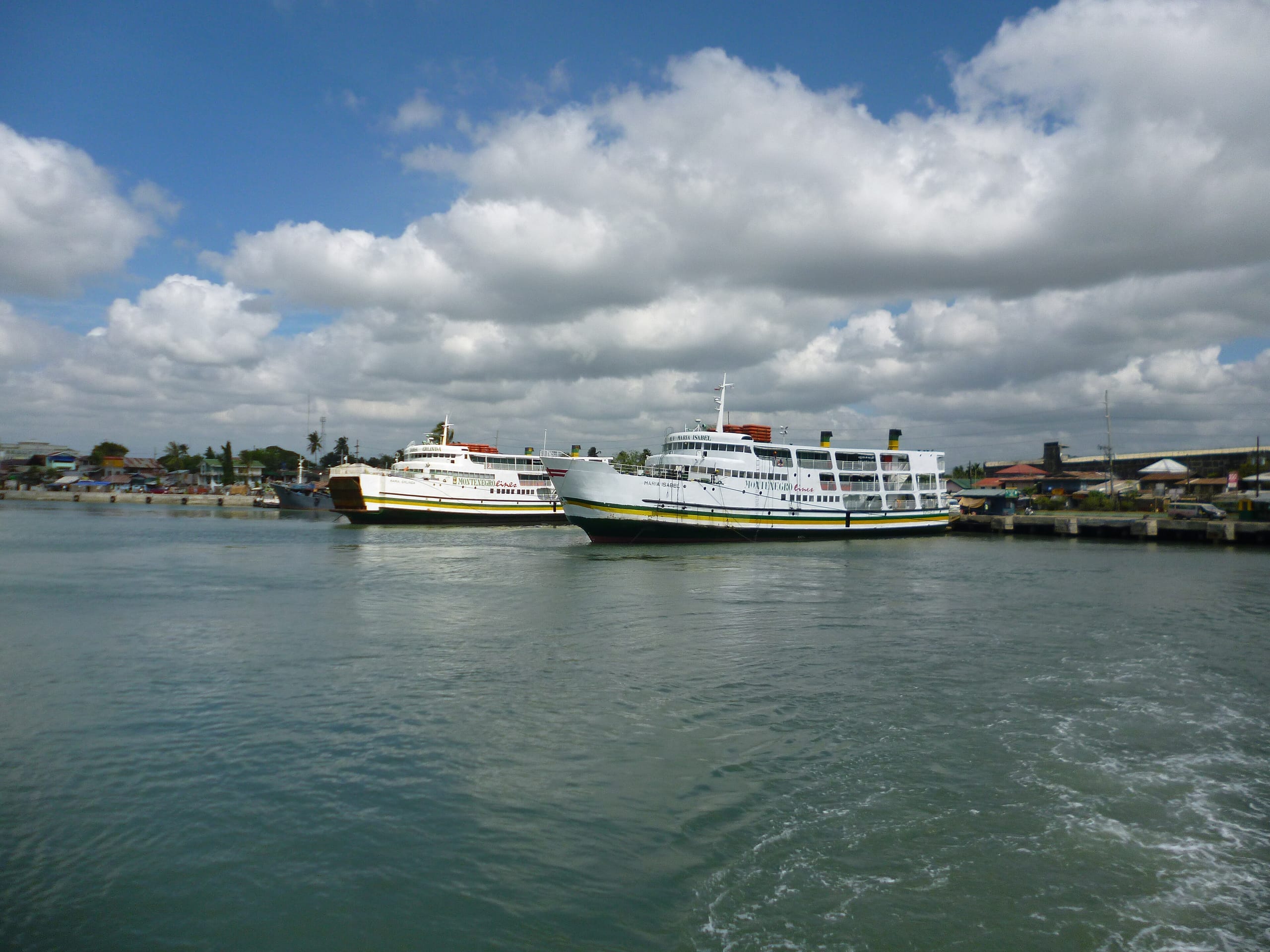 Two white Montenegro Lines ro-ro ferries moored at a pier in the Iloilo River under a cloudy sky