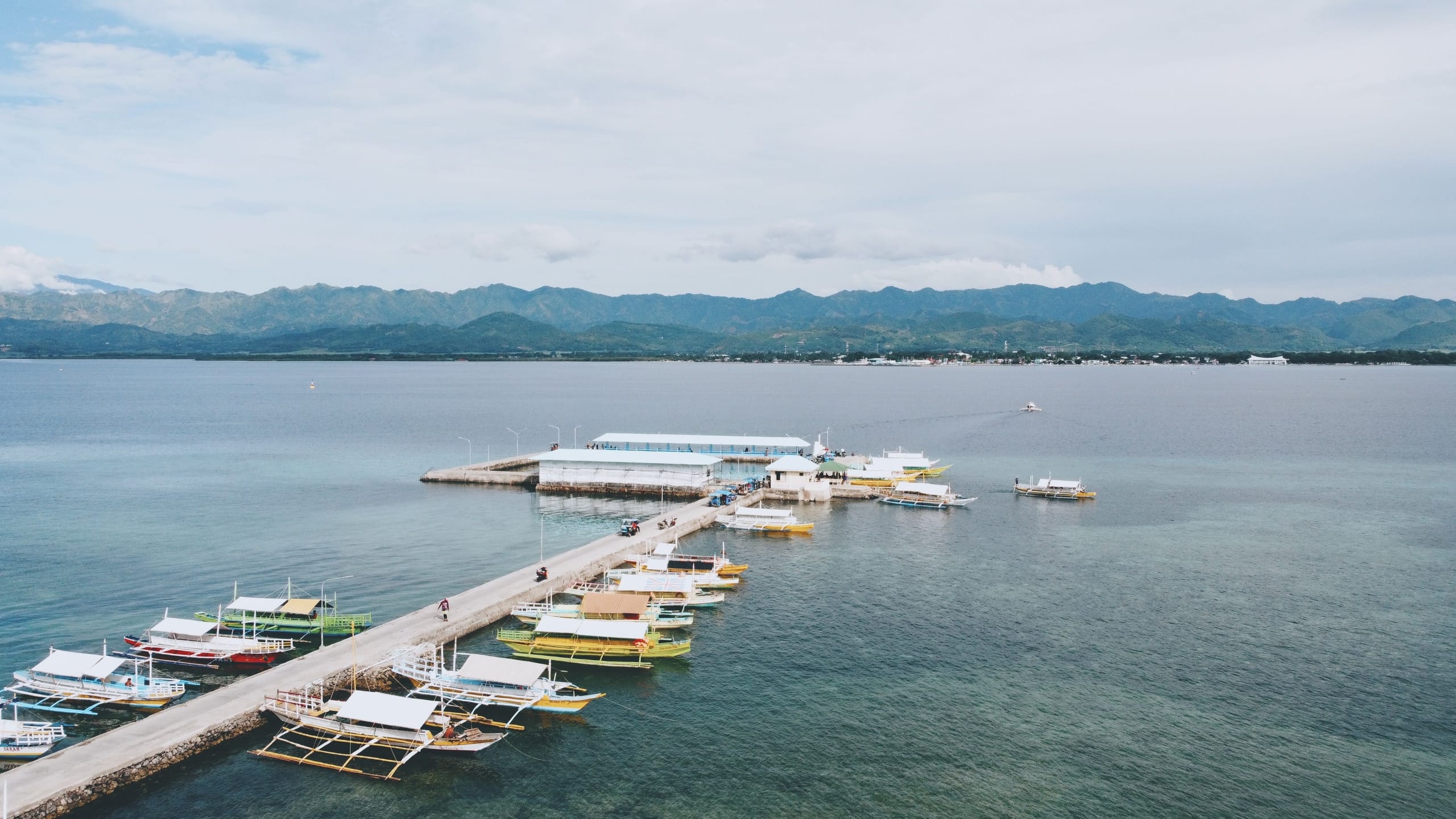 Boats tied up along a long pier at San Carlos City in the Philippines, the water flat and the far shore hazy