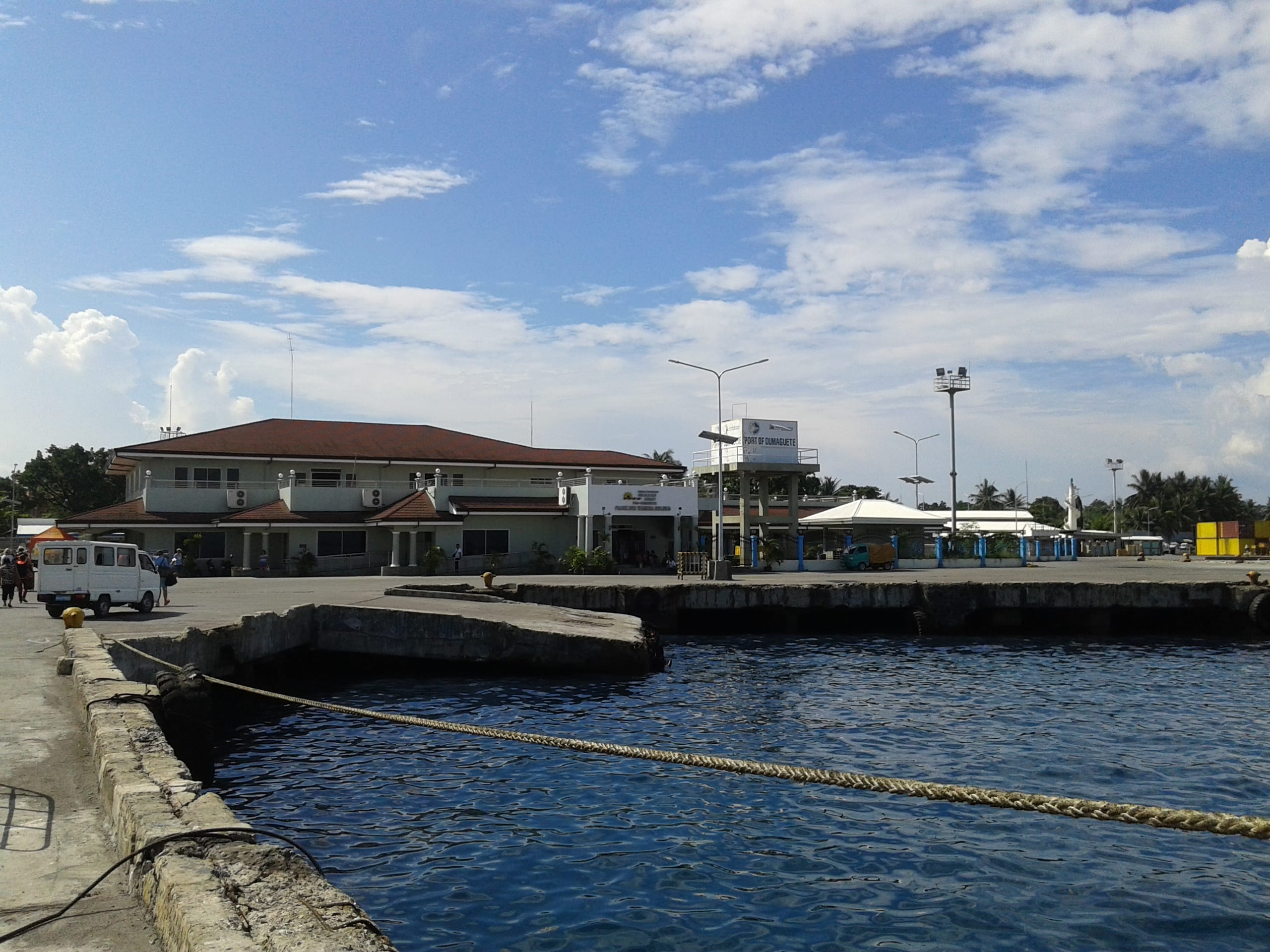 Passenger terminal building at the Dumaguete port seen across the water from the pier, a van parked at the quay