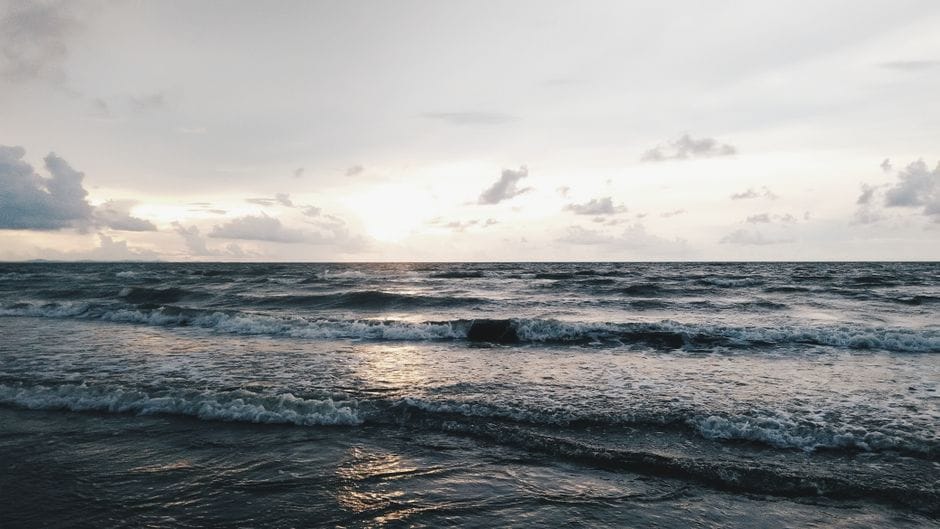 Rows of breaking waves running in to shore under a flat grey sky at first light