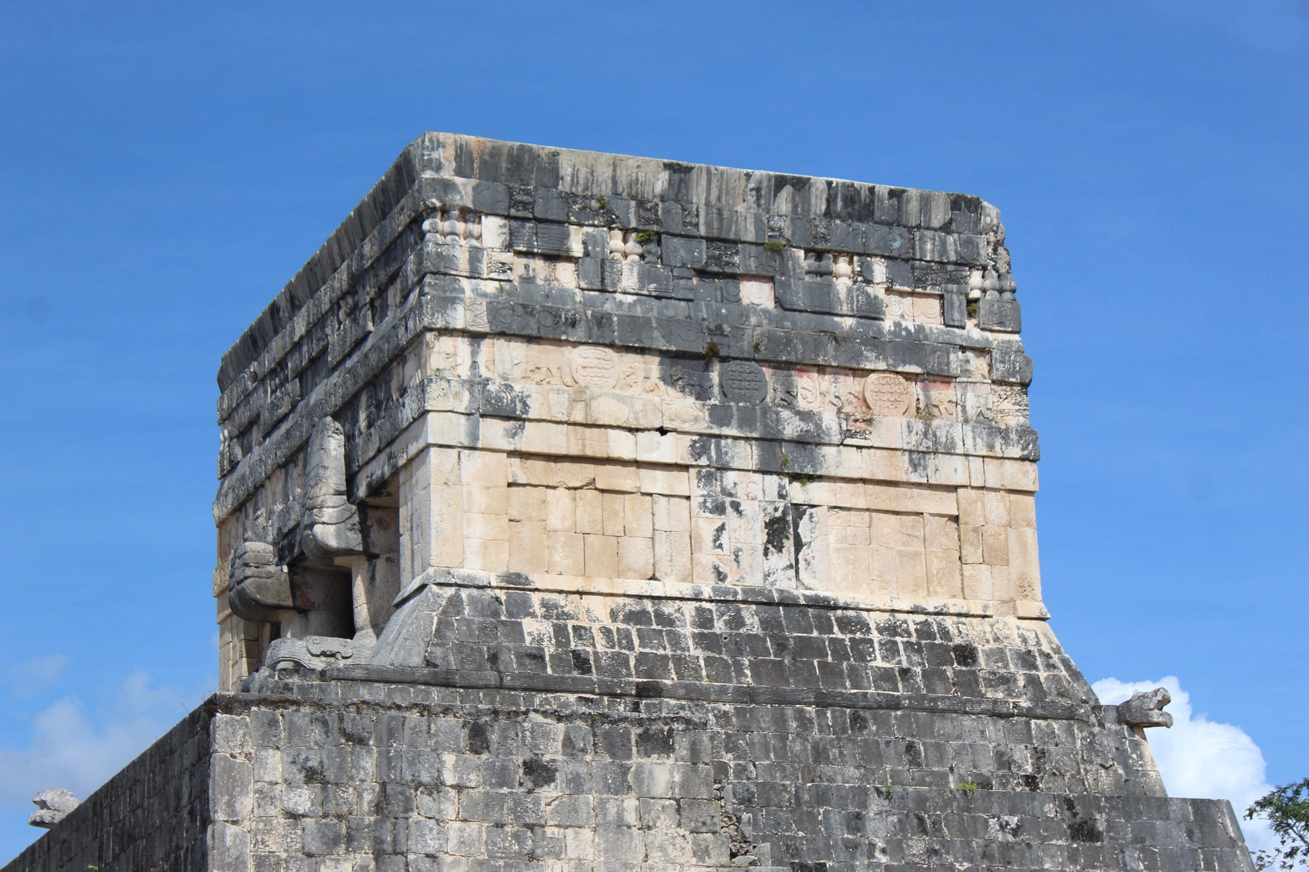 Weathered stone temple block with serpent heads at its corner on the Great Ball Court at Chichen Itza