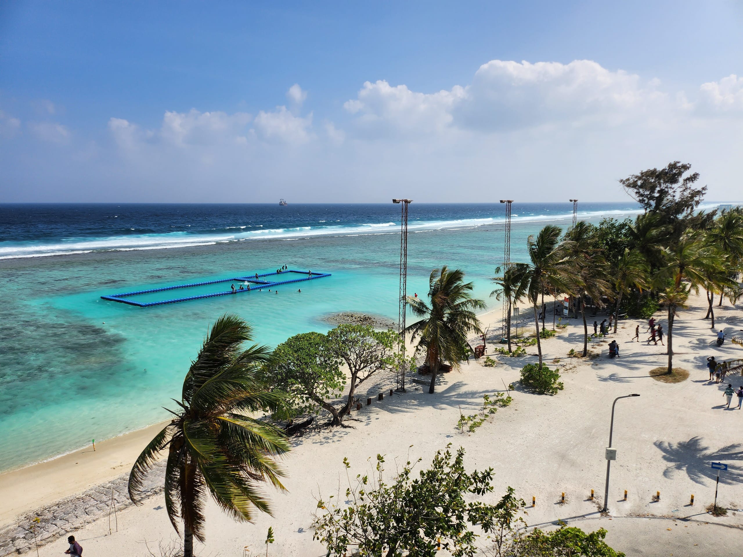 The city beach at Hulhumalé from above, palms on the sand and a floating swimming enclosure on the reef