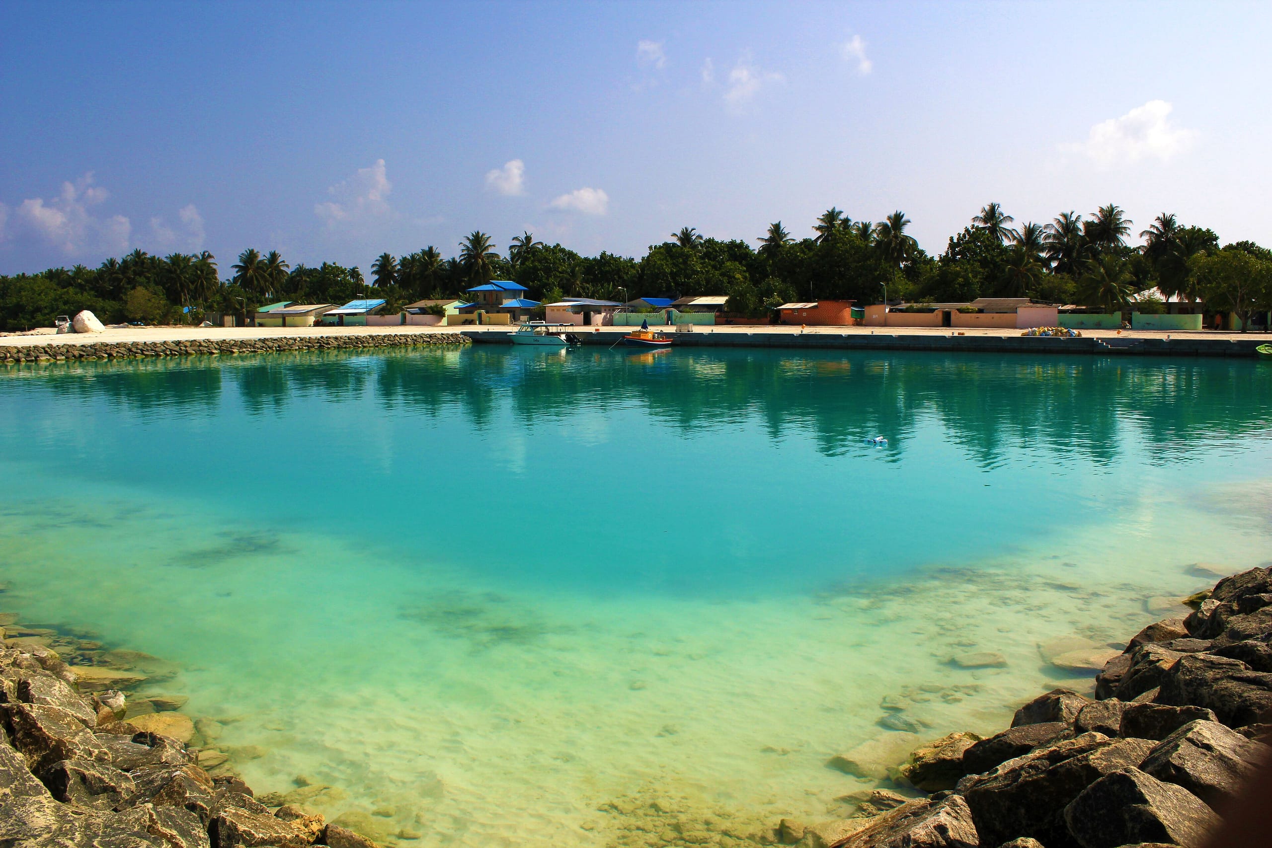 Low painted houses with blue roofs along the harbor wall at Ukulhas, seen from the front jetty