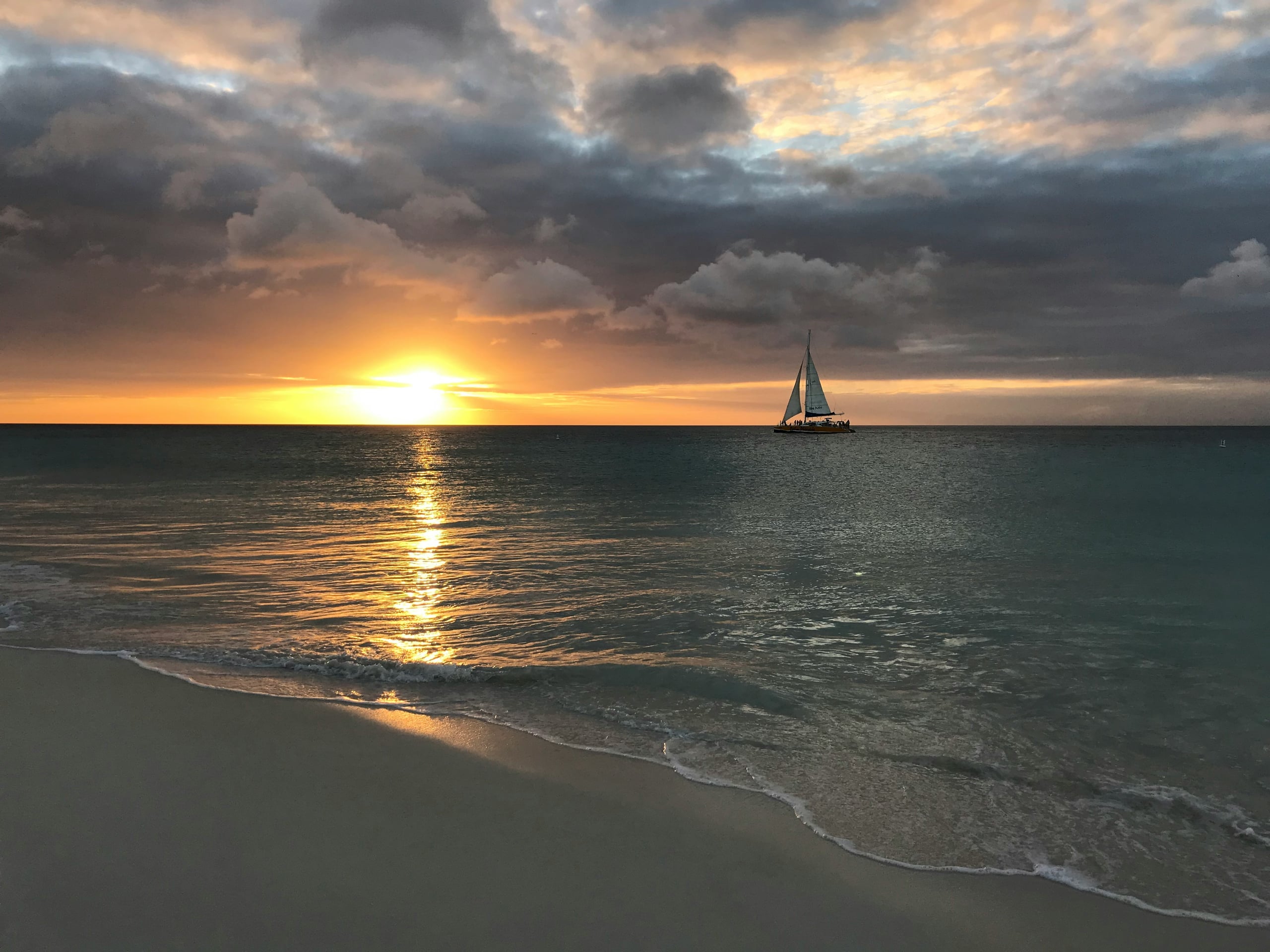 A catamaran on the horizon as the sun sets over Eagle Beach