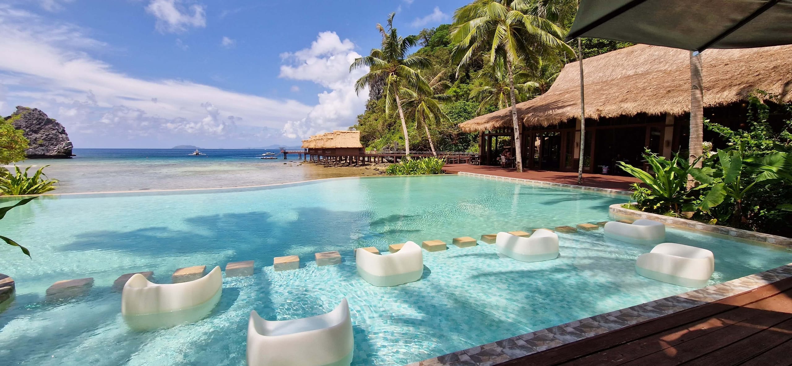 An infinity pool and loungers under a thatched roof on Cauayan Island, palms around it and open sea beyond