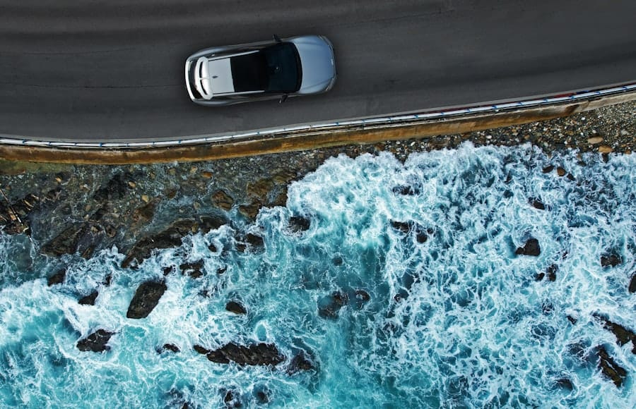 A car on a coastal road seen from above, with surf breaking on the rocks below