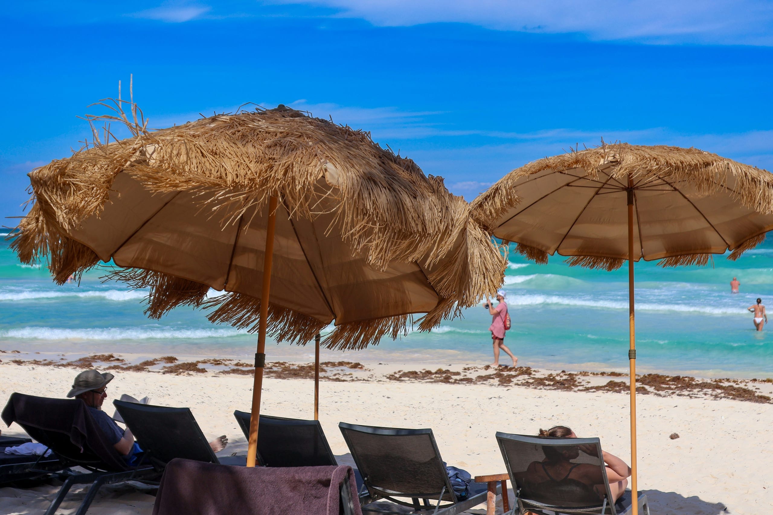 Thatched umbrellas and dark loungers set out on white sand with the sea turning turquoise behind them